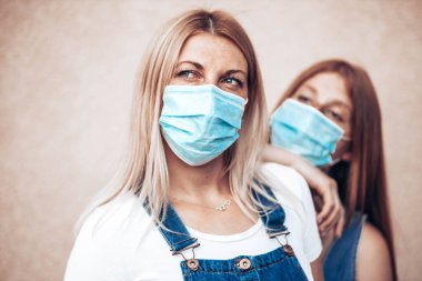 Yüz maskeli genç bir anne ve kız. Kızı annesine yaslanıyor, ona bakıyor.