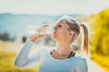 Sarışın, güçlü fit, sportif kadın sabah antrenmanından sonra su içiyor. Fitness, sağlıklı yaşam tarzı konsepti