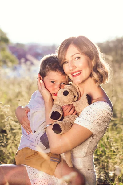 美しい若いお母さんは彼女の腕の中で彼女のブロンドの息子を保持する 屋外の写真 母の日 — ストック写真