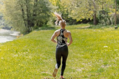 Arka planda spor giyerek koşan sarışın bir kızın fotoğrafı var.