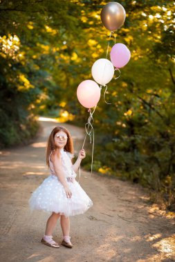 Küçük kızıl kafa balonları doğada tutuyor. Kutlama konsepti