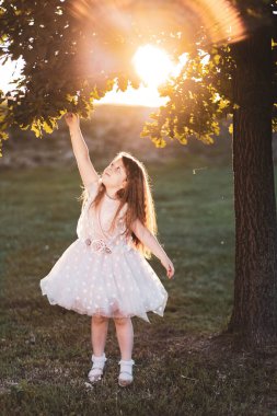 Mutlu kızıl kız parkta oynar, ağaç dalına tutunur