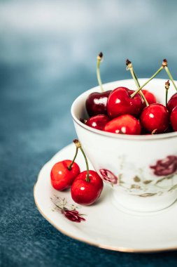 Masadaki porselen bardakta kırmızı, lezzetli kirazlar. Mavi arkaplan