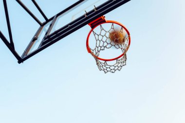 Kırmızı basketbol potasının alttaki görüntüsü. Top havada uçuşuyor. Boşluğu kopyala