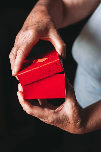 Close-up of elderly female hands opening red gift box. Black, dark background