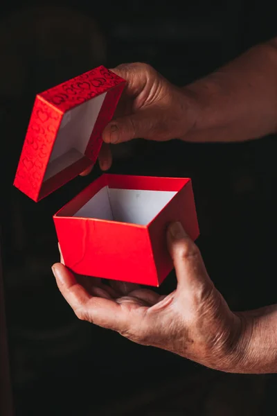 Close-up of elderly female hands opening red gift box. Black, dark background