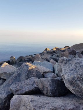 Mavi su ile taş deniz kıyısının güzel görünümü. Taşların üzerinde batan güneşten güzel bir gölge yatıyor.