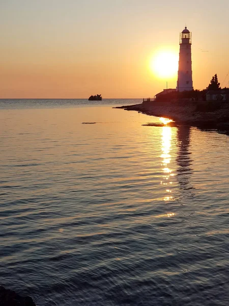 Tarkhankut deniz fenerinin, Karadeniz'in, bulutsuz bir yaz gününde batan sarı güneşin güzel manzarası. Kırım Cumhuriyeti