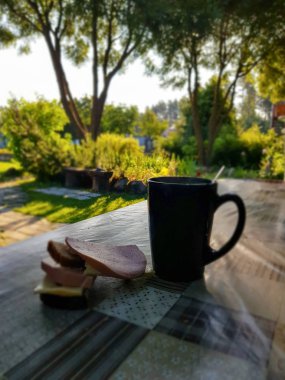 Sandviç ile bir fincan çay sabah yeşil bir bahçenin arka planında masada duruyor