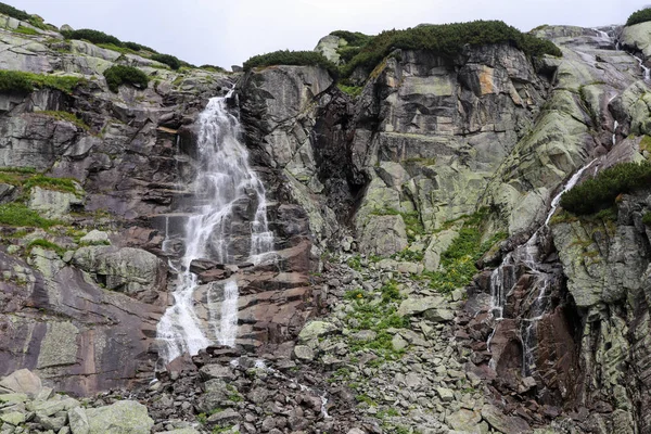 Cachoeira de montanha em High Tatras (Skok). Pedras altas cobertas de esfoliação. Grande cachoeira à esquerda, pequena água à direita . — Fotografia de Stock
