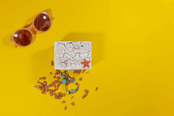 Gafas de sol, una caja, brazalete y rocas están colocadas en una superficie amarilla —  Fotos de Stock