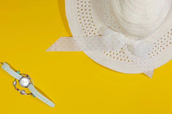 Biała czapka w prawym rogu układa się na żółtą powierzchnię z zegarkiem i bransoletką po lewej stronie — Zdjęcie stockowe