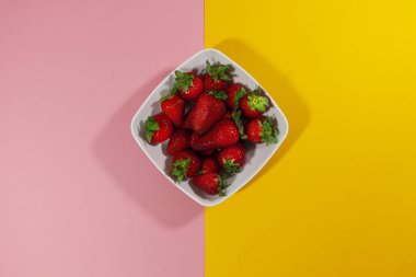 Pembe ve sarı yüzeyde bir kase çilek