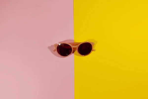 Gafas de sol colocadas en medio de una superficie rosa y amarilla — Foto de Stock