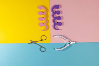 Tırnak makası, makas ve ayak ayırıcıları farklı renklerde düz bir yüzey üzerinde yatıyor: pembe, mavi ve sarı.