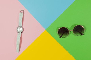 Beyaz saat ve siyah güneş gözlüğü sarı, yeşil, mavi ve pembe renk düz bir yüzey üzerinde döşeme
