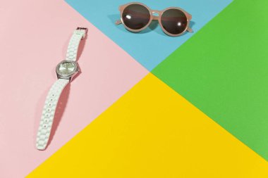 Beyaz saat ve siyah güneş gözlüğü sarı, yeşil, mavi ve pembe renk düz bir yüzey üzerinde döşeme