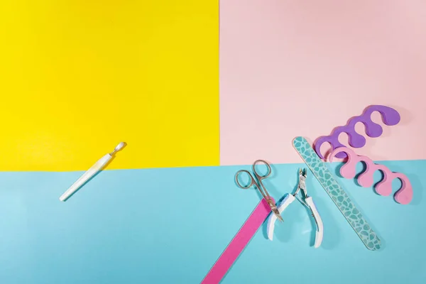 White nail clippers and two pairs of nail files, toe separators, and a cuticle device are laying on a flat surface with colors of pink, yellow, and blue — 스톡 사진