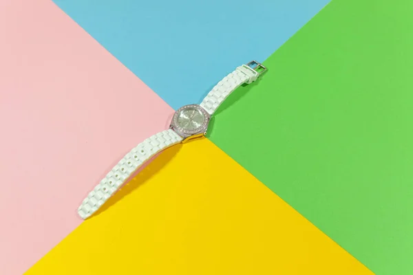 Un orologio bianco è disteso su una superficie piana di colore rosa, giallo, verde e blu — Foto Stock