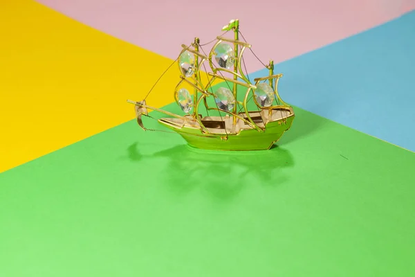 Een miniatuur gouden boot met edelstenen is het leggen op een plat oppervlak van verschillende kleuren groen, geel, roze en blauw — Stockfoto
