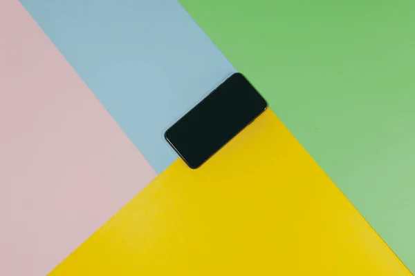 Un teléfono negro está tendido en una superficie plana de verde, azul, rosa y amarillo —  Fotos de Stock