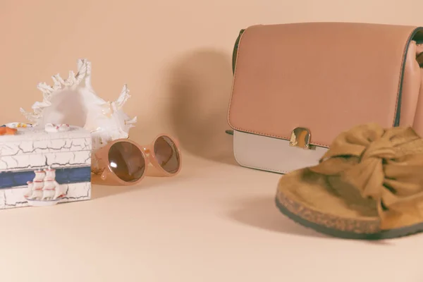 En handväska, sandaler, solglasögon, conch och Box är om på en rosa yta — Stockfoto