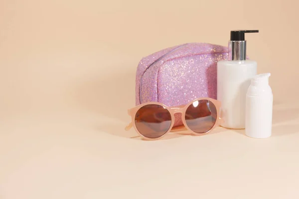 Eine rosa Kosmetiktasche, eine rosa Sonnenbrille und Lotionflaschen stehen auf einer rosafarbenen Oberfläche — Stockfoto
