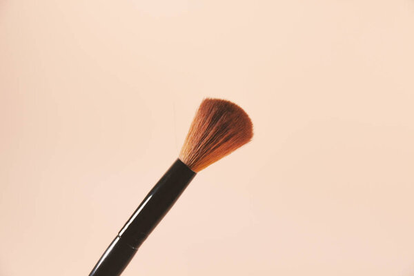A makeup brush is pictured in front of a pink background