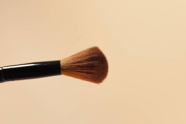 A makeup brush is pictured in front of a pink background