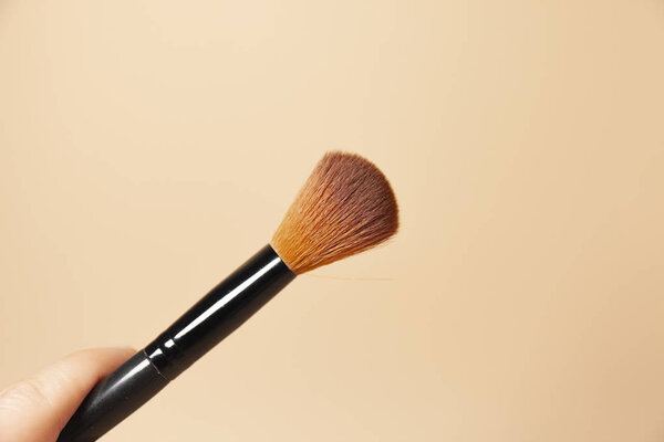 A makeup brush is pictured in front of a pink background