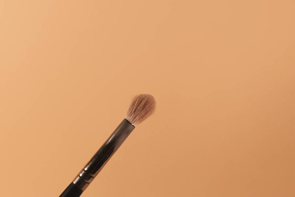 A makeup brush is pictured in front of a pink background