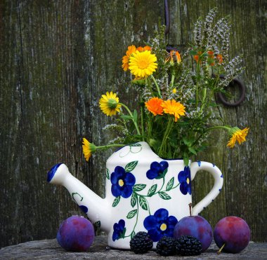 Porselen bir çaydanlıkla hayat. Calendula ve nane çiçekleri, erikler ve böğürtlenler.