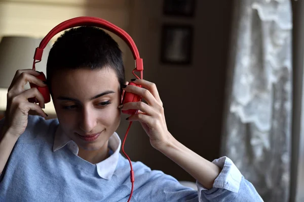 Kırmızı kulaklıklı genç bayan evde müzik dinlemeye hazırlanıyor.