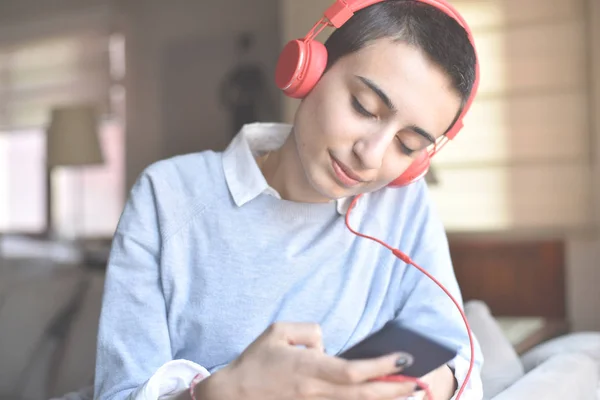 Kırmızı kulaklıklı genç bayan evde müzik dinlemeye hazırlanıyor.