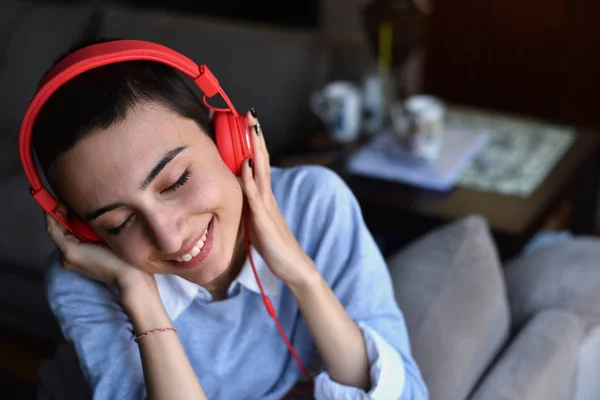Kırmızı kulaklıklı genç bayan evde müzik dinlemeye hazırlanıyor.