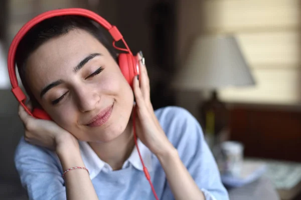 Kırmızı kulaklıklı genç bayan evde müzik dinlemeye hazırlanıyor.