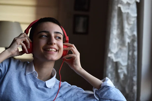 Kırmızı kulaklıklı genç bayan evde müzik dinlemeye hazırlanıyor.