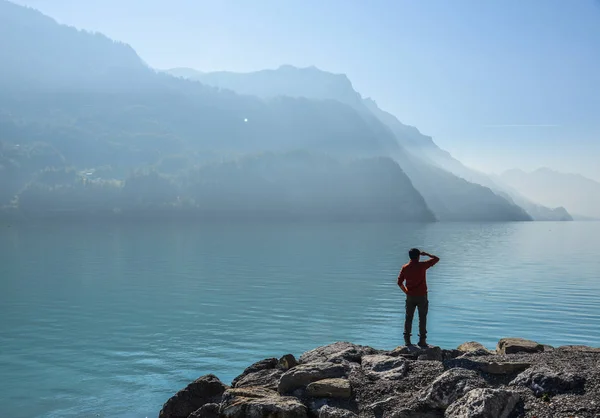 A young man standing on rock near lake in Brienz, Switzerland. The turquoise Lake Brienz is set amid the spectacular mountain scenery.