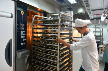 Saigon, Vietnam - 9 Ocak 2018. Taze pişmiş ekmek rafları ile Saigon (Ho Chi Minh City), Vietnam fabrikasında çalışan bir erkeğin.