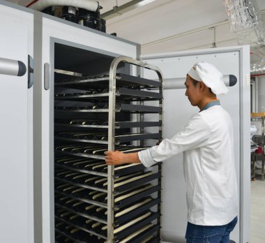 Saigon, Vietnam - 9 Ocak 2018. Taze pişmiş ekmek rafları ile Saigon (Ho Chi Minh City), Vietnam fabrikasında çalışan bir erkeğin.