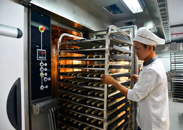Saigon, Vietnam - 9 Ocak 2018. Taze pişmiş ekmek rafları ile Saigon (Ho Chi Minh City), Vietnam fabrikasında çalışan bir erkeğin.