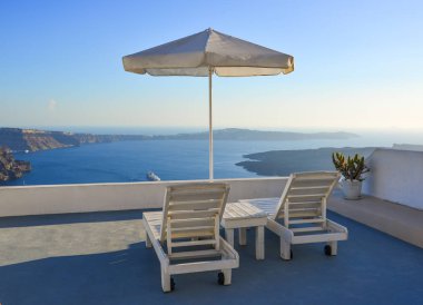 Yaz aylarında Santorini Adası'nda dinlendirici sandalye ve beyaz villa şemsiyesi ile Seaview balkon.