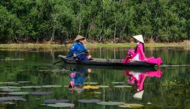 Binh Duong, Vietnam - 4 Şubat 2016. Asyalı kadın geleneksel elbise (Ao Dai) Nilüfer gölet ahşap teknede oturuyor.