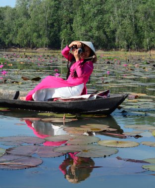 Binh Duong, Vietnam - 4 Şubat 2016. Asyalı kadın geleneksel elbise (Ao Dai) Nilüfer gölet ahşap teknede oturuyor.