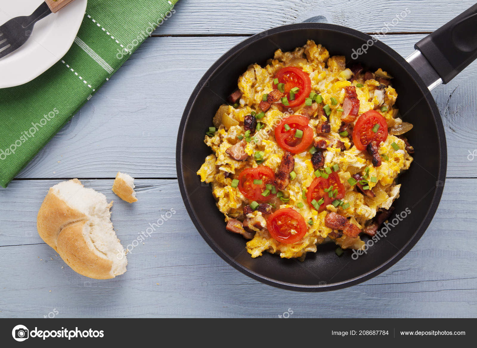 Scrambled eggs in a pan with bacon, onion and tomatoes sprinkled Stock