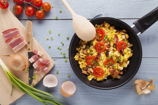 Scrambled eggs in a pan with bacon, onion and tomatoes sprinkled — Stock Photo, Image