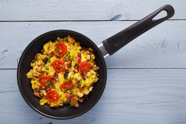 Scrambled eggs in a pan with bacon, onion and tomatoes sprinkled — Stock Photo, Image