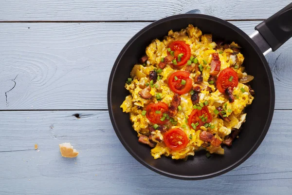 Scrambled eggs in a pan with bacon, onion and tomatoes sprinkled — Stock Photo, Image