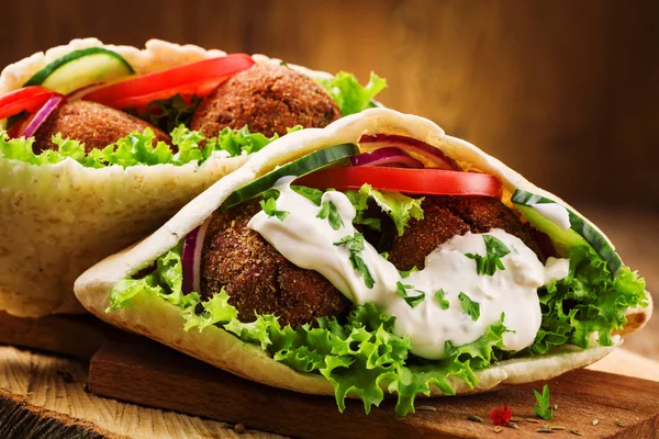 Falafel i świeże warzywa w chlebie pita na drewnianym stole — Zdjęcie stockowe