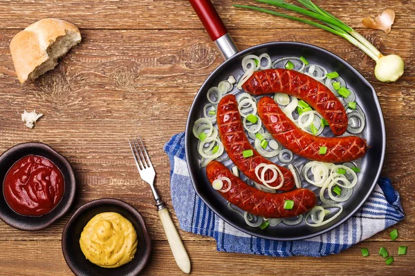 Bratwürste in der Pfanne mit Zwiebeln. — Stockfoto